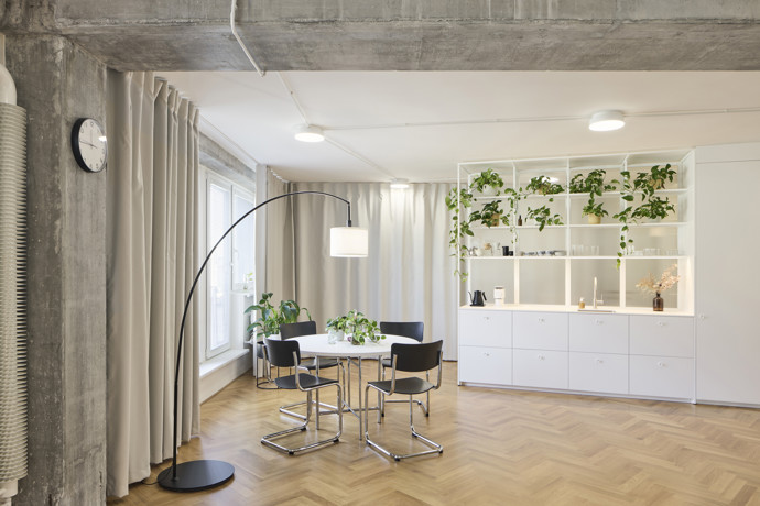 Na první pohled působí tento byt překvapivě jednoduše. Když se ale člověk začne rozhlížet, zjistí, že nic není náhoda. Architekti se rozhodli opustit tradiční dělení na jednotlivé místnosti a vytvořili domov, kde hranice mezi kuchyní, obývacím pokojem, pracovnou nebo ložnicí nejsou pevně dané zdmi, ale spíš způsobem používání prostoru. 