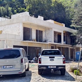 Na stavbě v Divoké Šárce je čilý ruch, před vznikající vilou parkují auta dělníků a stavebních firem.