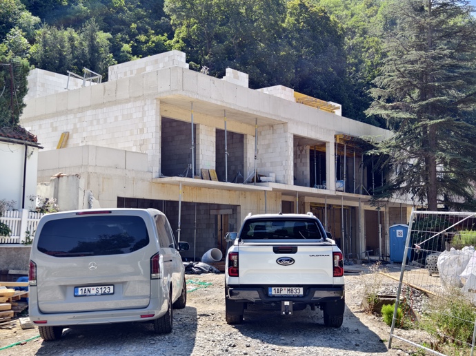 Na stavbě v Divoké Šárce je čilý ruch, před vznikající vilou parkují auta dělníků a stavebních firem.