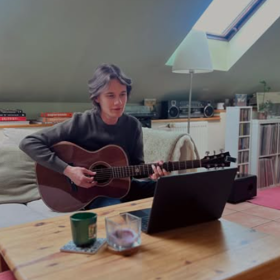 Frontman Stevens piluje kytarové riffy na pohovce s notebookem.