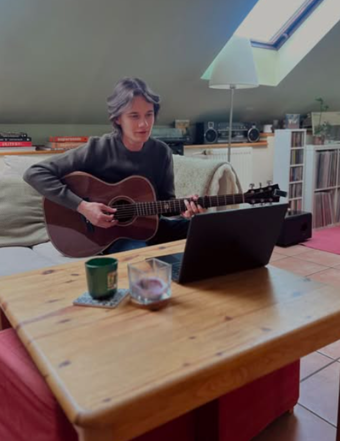 Frontman Stevens piluje kytarové riffy na pohovce s notebookem.