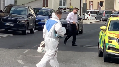 FOTO: Kriminalistický technik v ochranném obleku vynáší z domu kufry s důkazy.