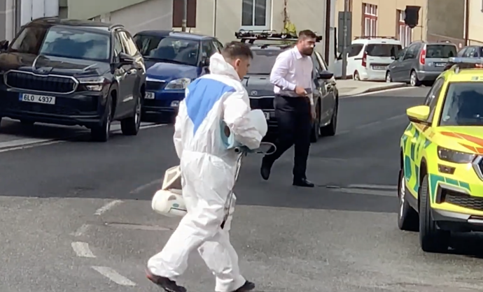 Kriminalistický technik v ochranném obleku vynáší z domu kufry s důkazy.
