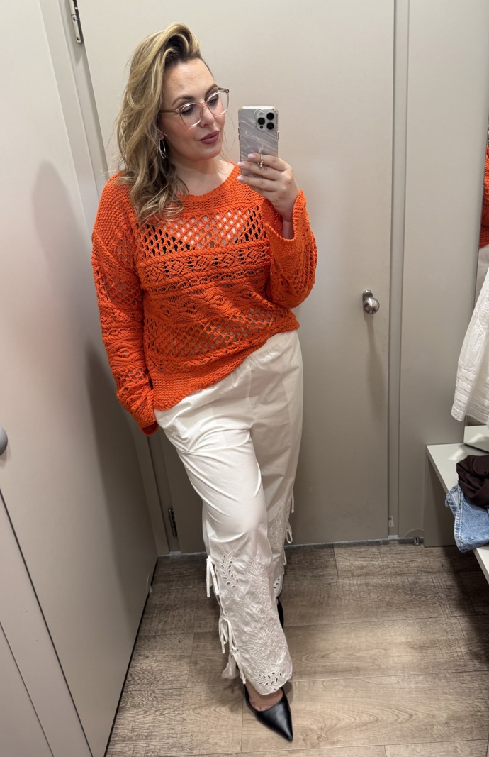Lehký svetřík syté oranžové barvy z výprodeje Marks& Spencer koupíte za 749 Kč. Bílé kalhoty s madeirou a vázáním na lýtku za 699 Kč.
