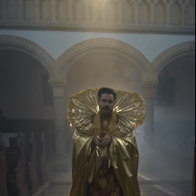 Extravagantní zlaté roucho s vysokým límcem vyráží dech.