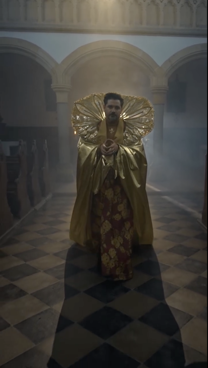 Extravagantní zlaté roucho s vysokým límcem vyráží dech.