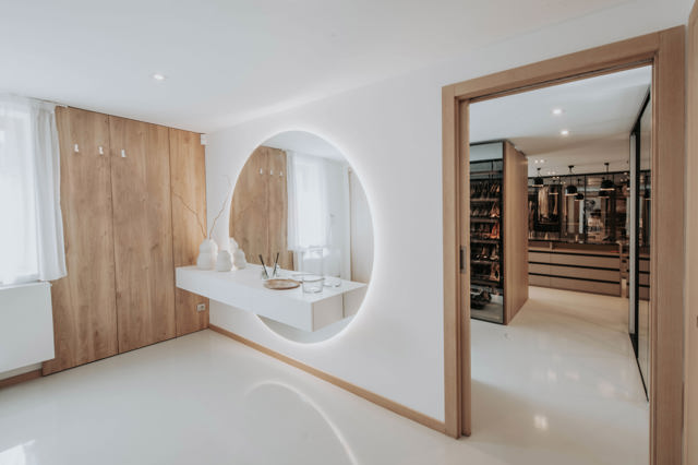 Vstupní část je velmi střídmá, ale velké kulaté zrcadlo, dřevěná stěna a pohled do šatny jí dodávají elegantní hotelovou atmosféru
