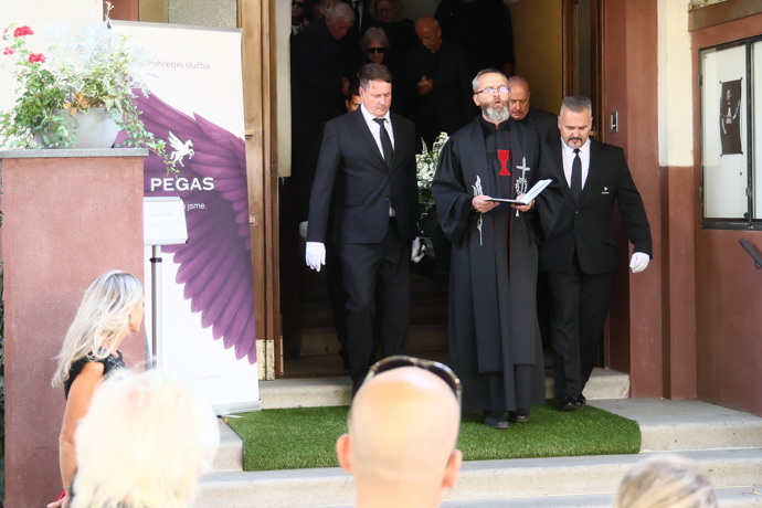 Rakev byla vynesena ven v čele s knězem. 