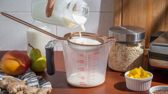 Ruční nalévání mléka přes sítko s kefírovými zrny