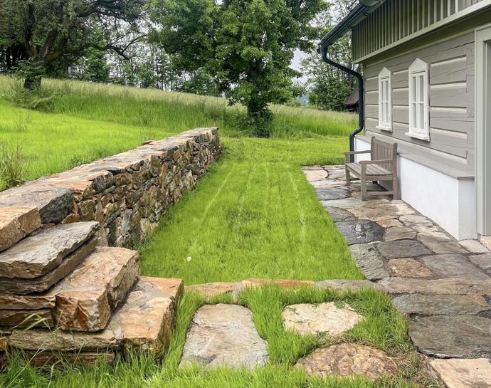 Okolí domu zůstává přirozené a nenápadné, kamenné zídky a travnaté plochy navazují na původní ráz místa