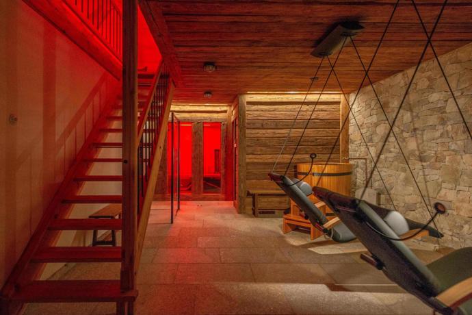 Wellness zóna má mnohem intimnější atmosféru, kterou vytváří tlumené červené světlo, dřevo, kamenná stěna a závěsná relaxační lehátka