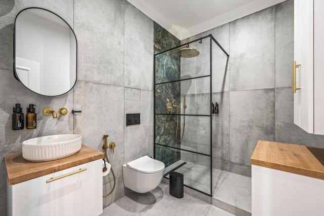 Koupelna staví na velkoformátových šedých obkladech, černém rámu sprchy a mosazných bateriích Koupelna staví na velkoformátových šedých obkladech, černém rámu sprchy a mosazných bateriích